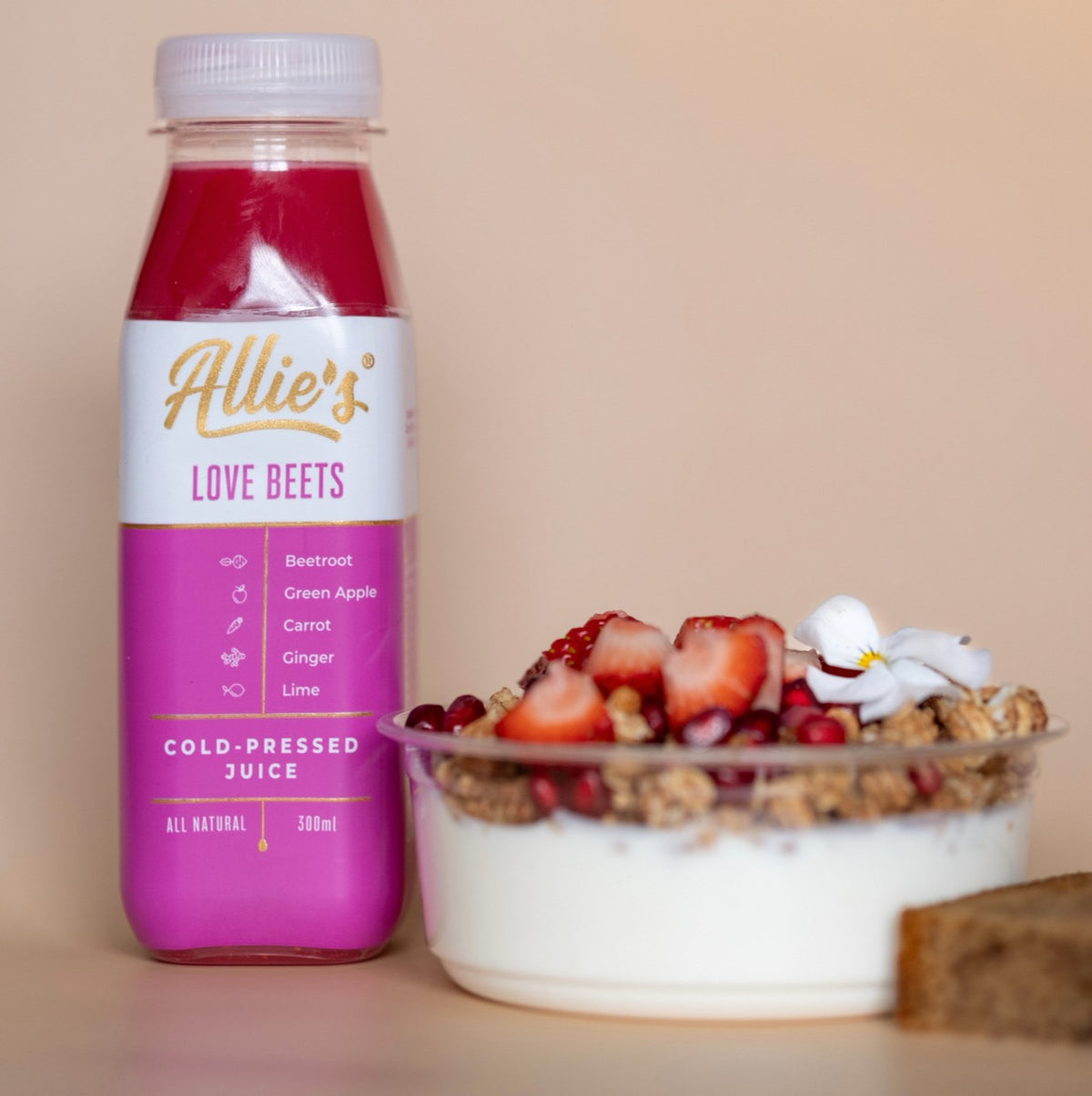Allie’s Love Beets juice beside yoghurt topped with granola, strawberries and an edible flower.
